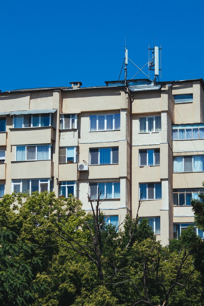 services-02 A beige apartment building surrounded by lush green trees under a clear blue sky.