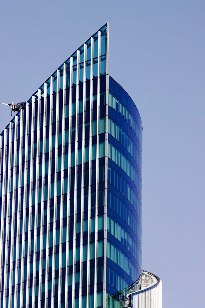 who-we-are Tall modern glass skyscraper with unique angles against a clear blue sky.