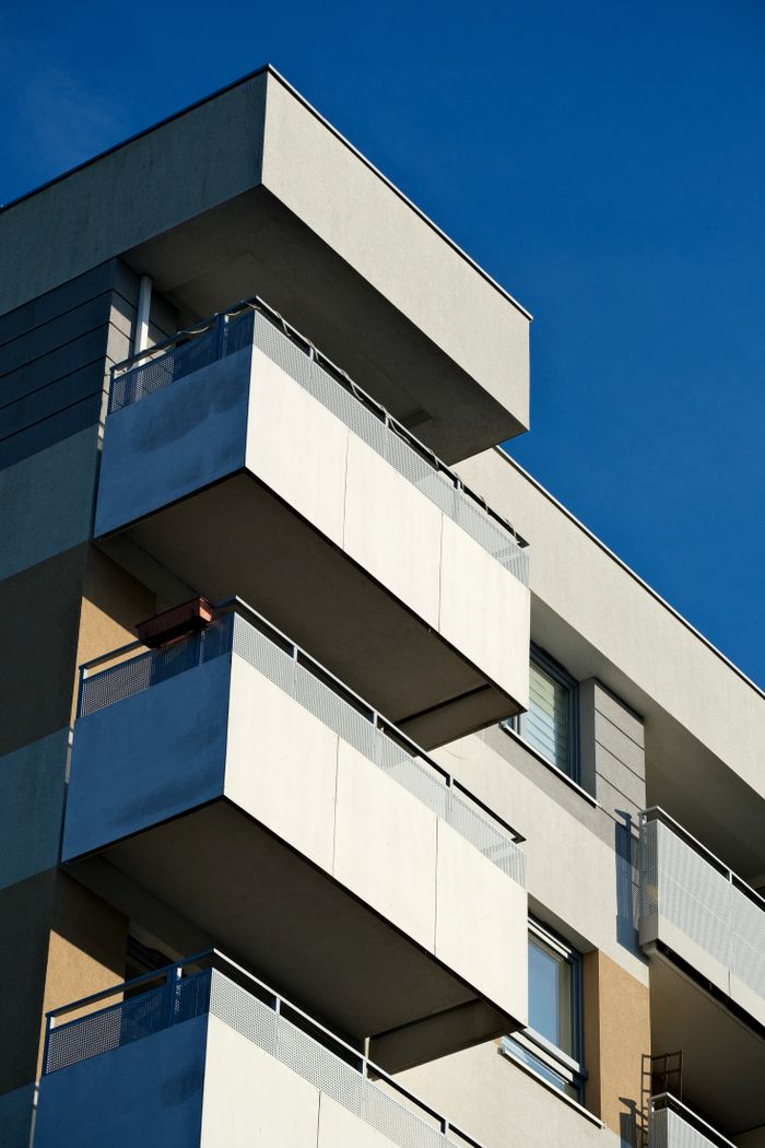 services-04 Close-up of a modern apartment building showcasing minimalist design against a clear blue sky.
