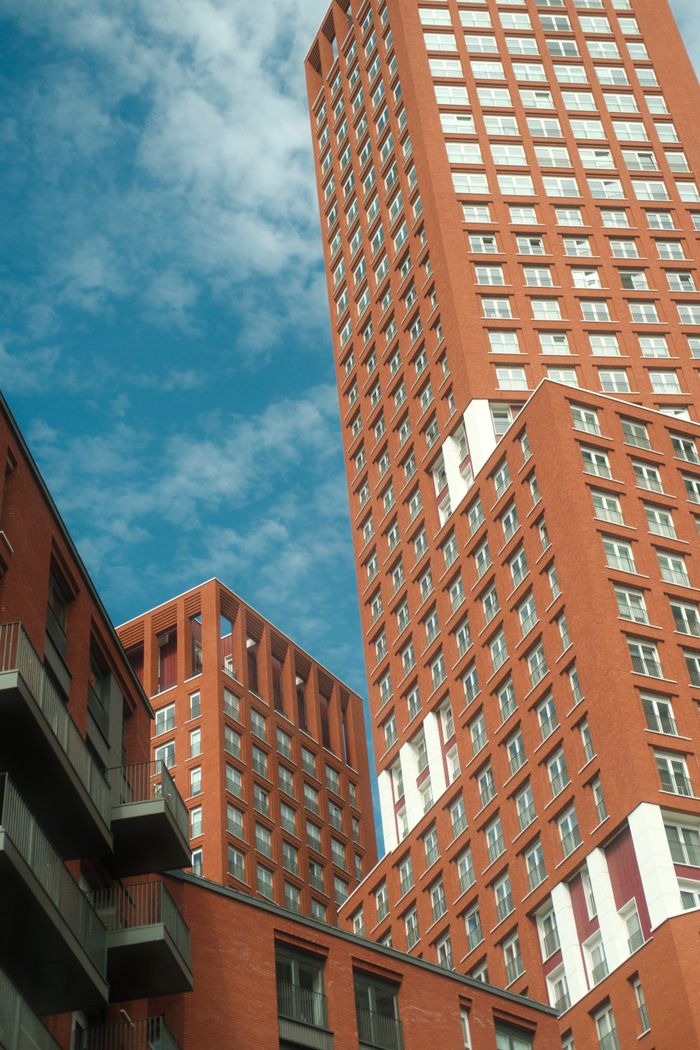 services-01 A view of modern red brick skyscrapers reaching towards a clear blue sky, showcasing urban architecture.
